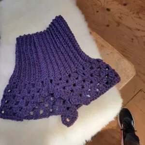 A purple hand-knit neck warmer on a wool blanket